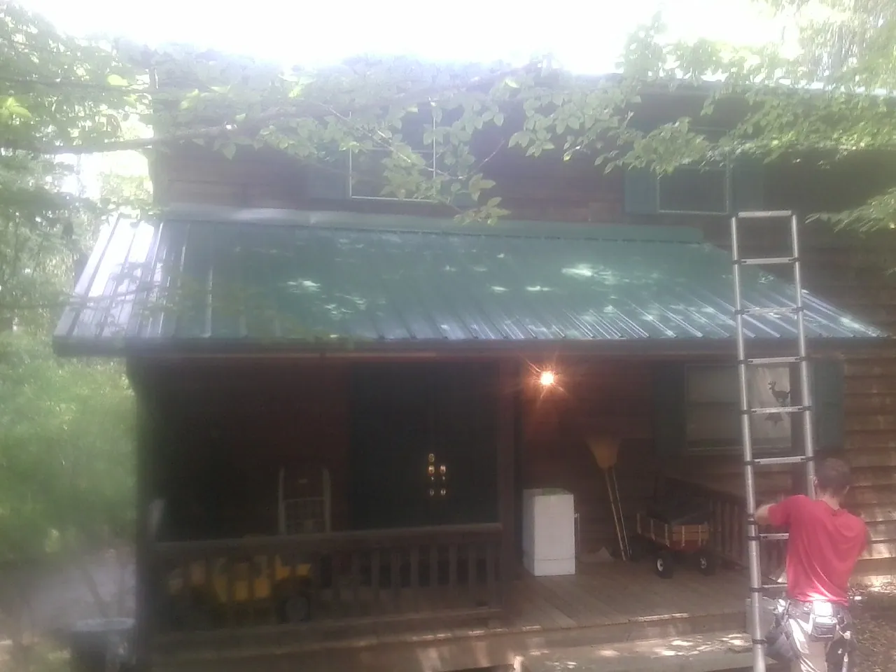 Worker on a ladder at the green porch roof of a wooded cabin in Weehawken