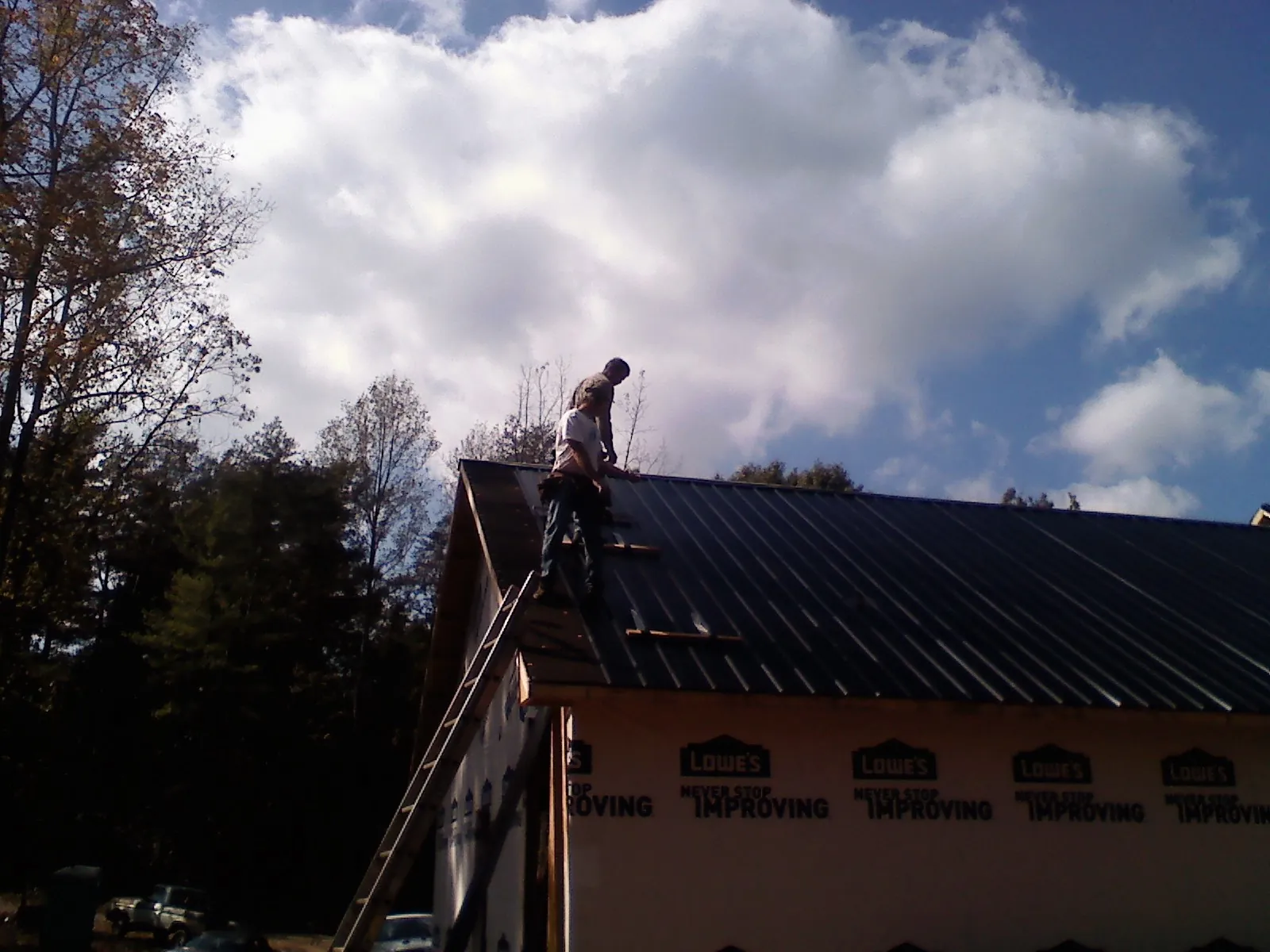 Roofer fastening dark metal panels high against a cloudy sky, from a Roof Inspection job in Weehawken