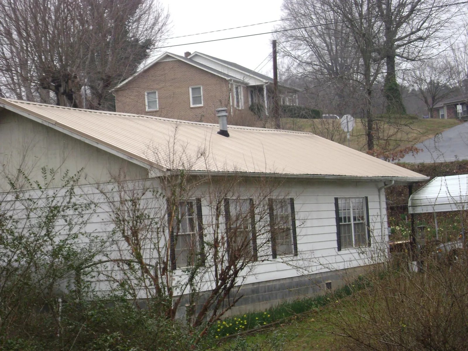 Tan metal roof on a white sided house set into a hillside — Commercial Roofing by Roofing Brothers in Weehawken